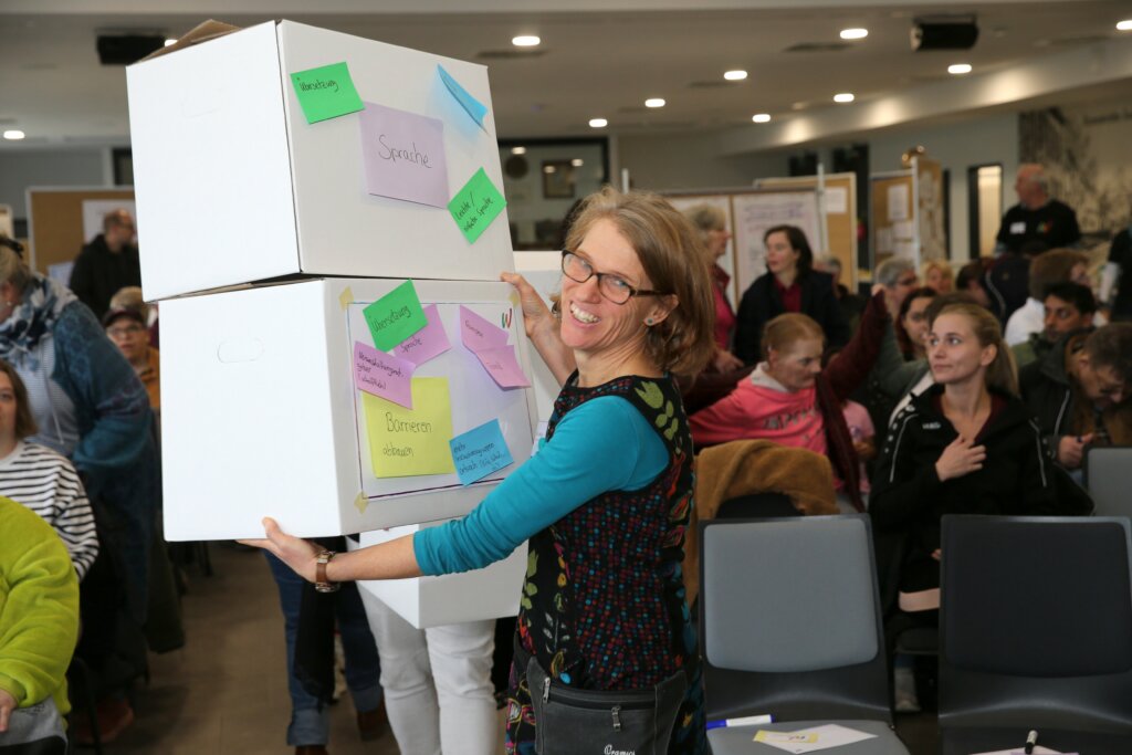 Eine Frau hält zwei gestapelte Kartons in den Händen. Auf den Kartons stehen Ergebnisse der Gruppenarbeit