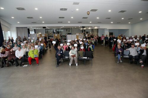 Viele Menschen sitzen im Publikum im Saal des Stadtteilhauses und halten Zettel mit ihren W&uuml;nschen hoch.