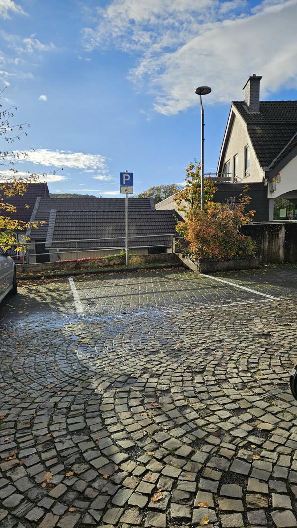 Das Bild zeigt einen Rollstuhlparkplatz. Der Untergrund ist aus Kopfsteinpflaster