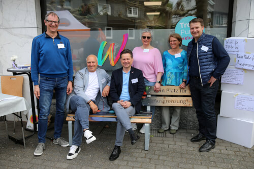 Gruppenfoto Das BIld zeigt eine Gruppe von 6 Personen die sich um die Bank gegen Ausgrenzung aufgestellt haben oder darauf sitzen