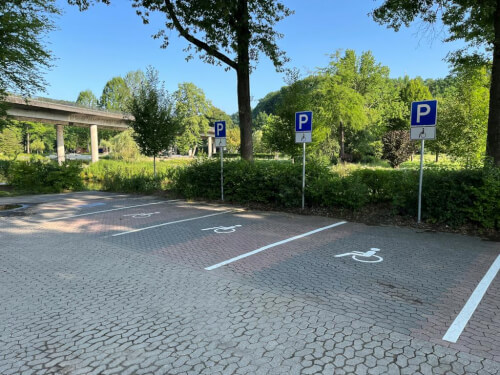 Barrierefreier Parkplatz 2 Vier Parkplätze für Menschen mit Behinderungen sind mit Schildern und Bodensymbolen gekennzeichnet und befinden sich auf einem Parkplatz neben Bäumen und Grünflächen unter freiem Himmel.