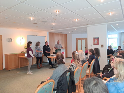Eine Gruppe von Personen sitzt während einer Präsentation vor einer Gruppe von vier Rednern, die vorne in einem Konferenzraum stehen.
